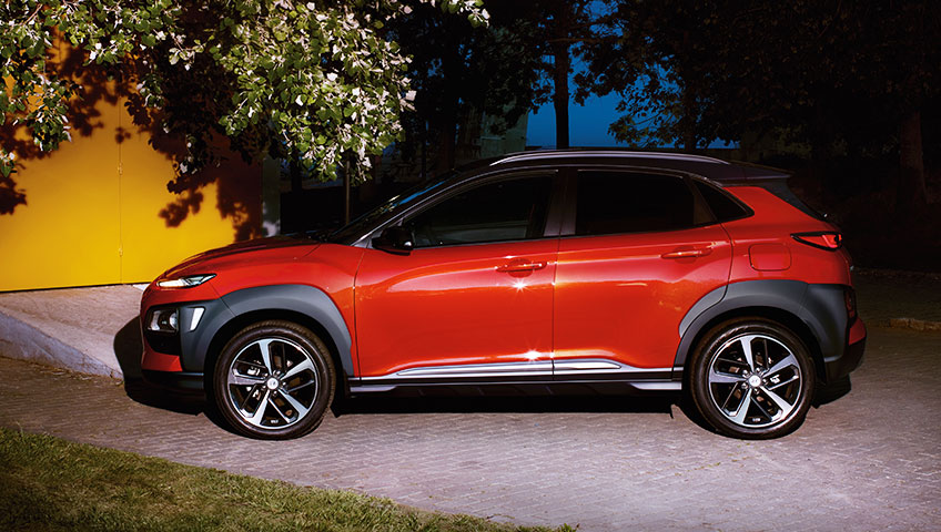 Left side view of red kona parked on the road.